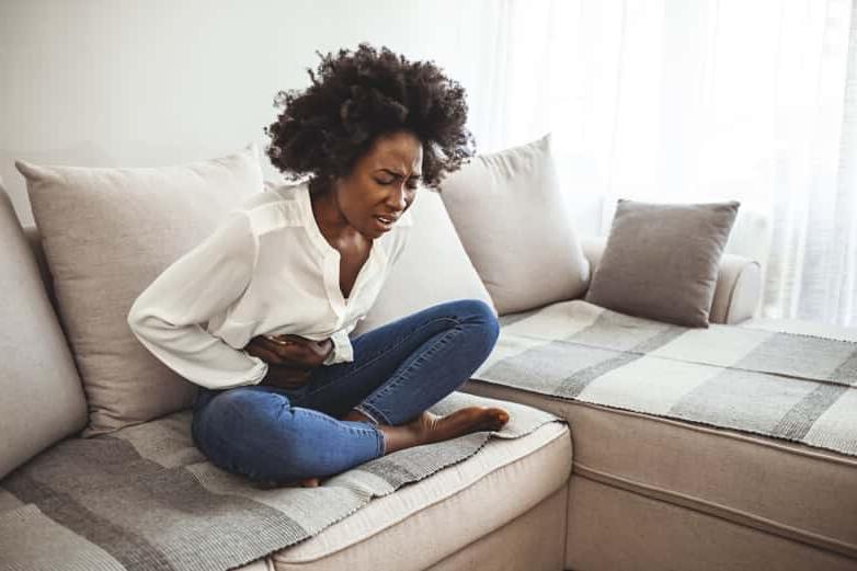 Black woman with period and 盆腔痛, holding her stomach.